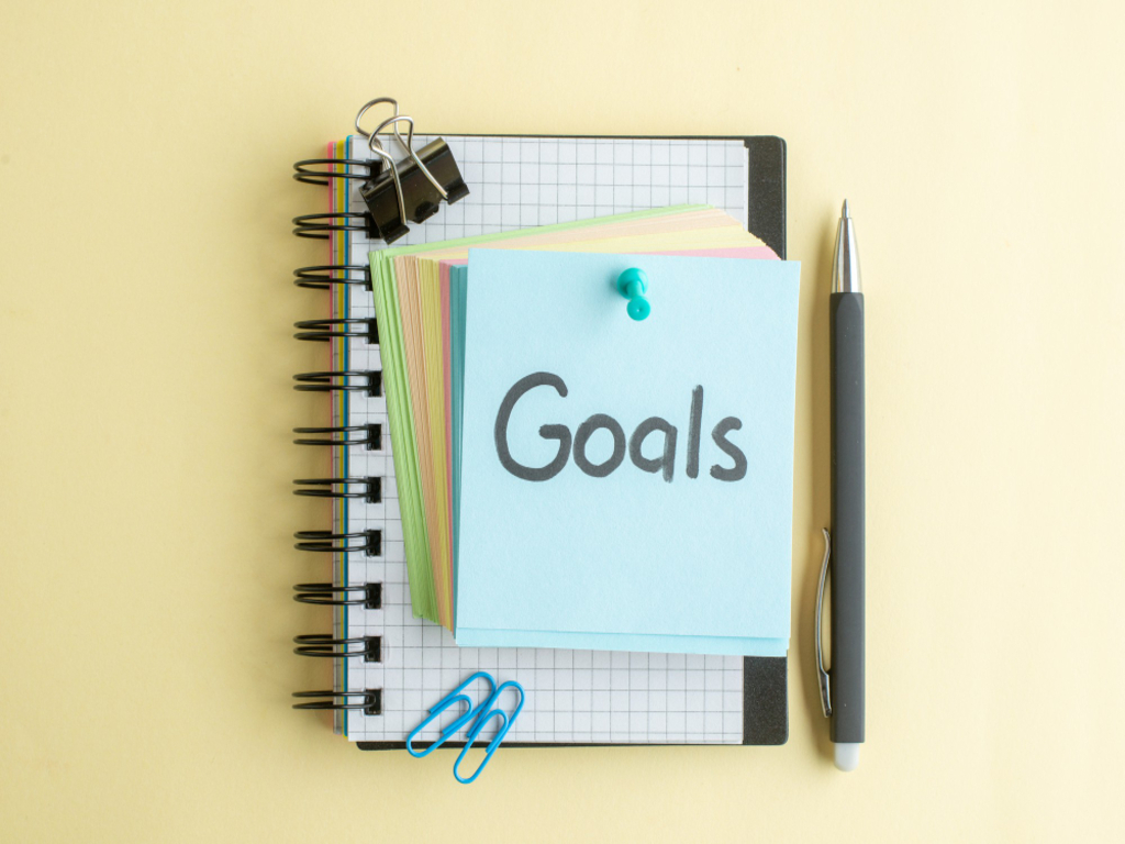 Visual of a person working at a desk with a laptop and sticky notes on the wall, symbolizing a commitment to focus on goals through effective planning and organization.